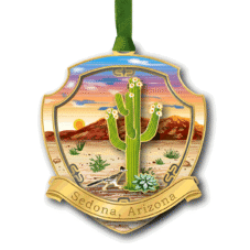Gold badge ornament with a desert scene: tall cactus, sunset sky, mountains, and a 'Sedona, Arizona' ribbon.