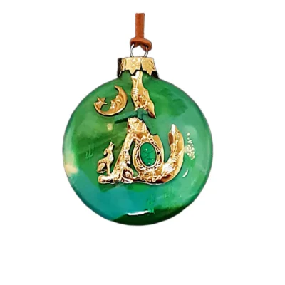 Emerald green glass Southwest ornament featuring a gold howling wolf emblem set with a green oval cabochon, green suede tie, smaller howling wolf, and crescent moon with star.