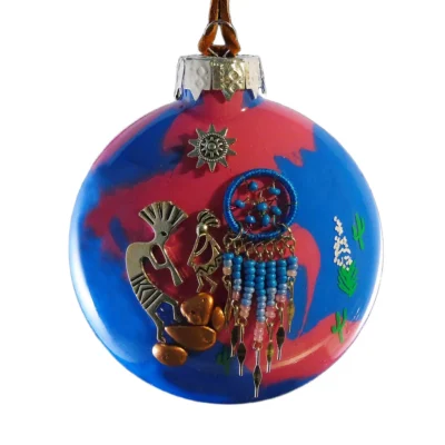 Southwest glass ornament featuring metallic Kokopelli figures, a blue beaded dreamcatcher, and cactus accents on a pink and blue background.
