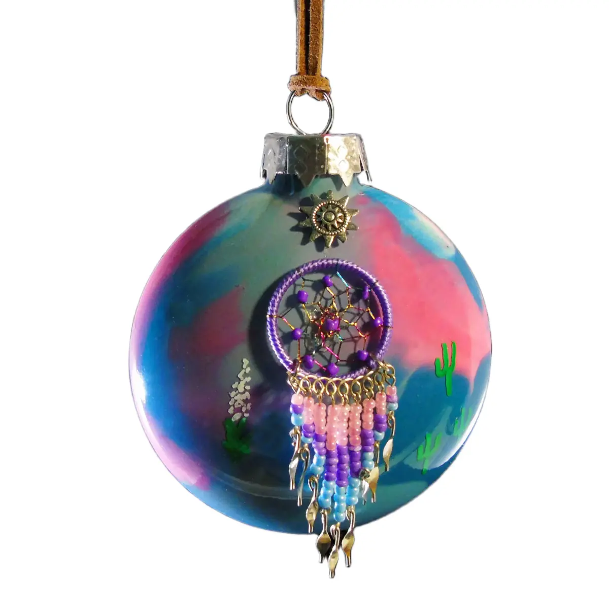 Pink and blue glass Southwest ornament featuring a purple webbed dreamcatcher with pink, purple, and light blue beaded tassels, sun charm, and desert cacti.