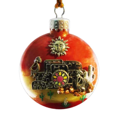 Metallic red and copper glass Southwest ornament featuring an orange webbed dreamcatcher with orange and black beaded tassels, sun charm, and desert cacti.