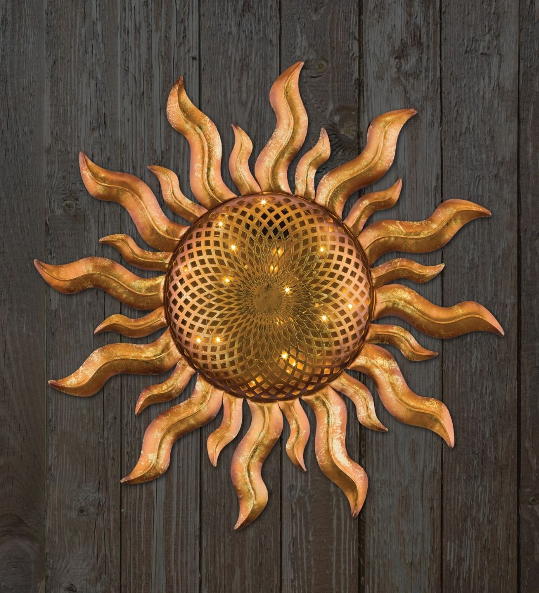 Gold sunburst wall decoration with a woven center mounted on dark wooden planks of a wall.