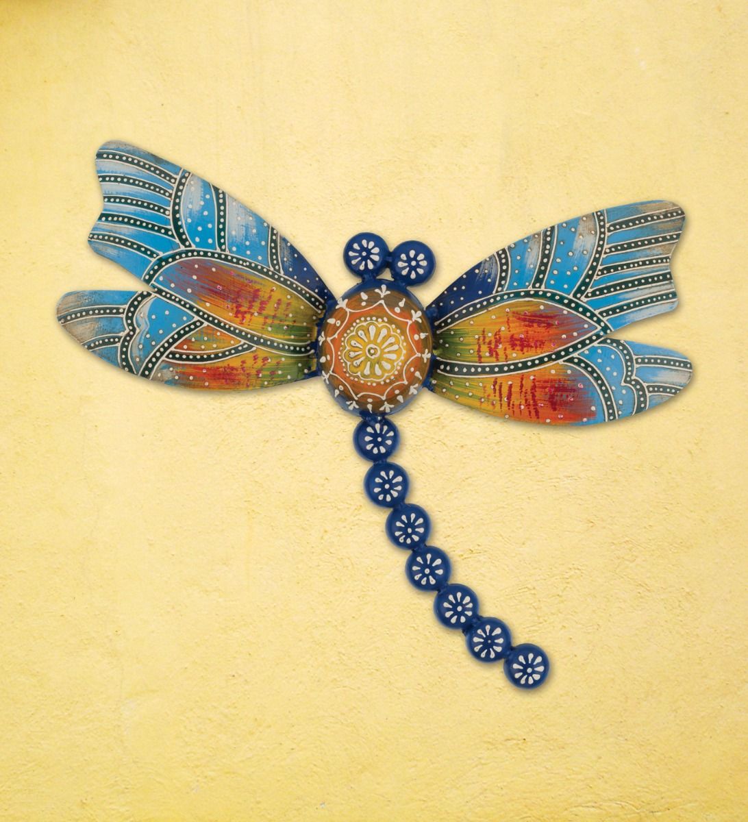 Decorative dragonfly wall art with multicolored patterned wings and a blue beaded tail on a yellow wall