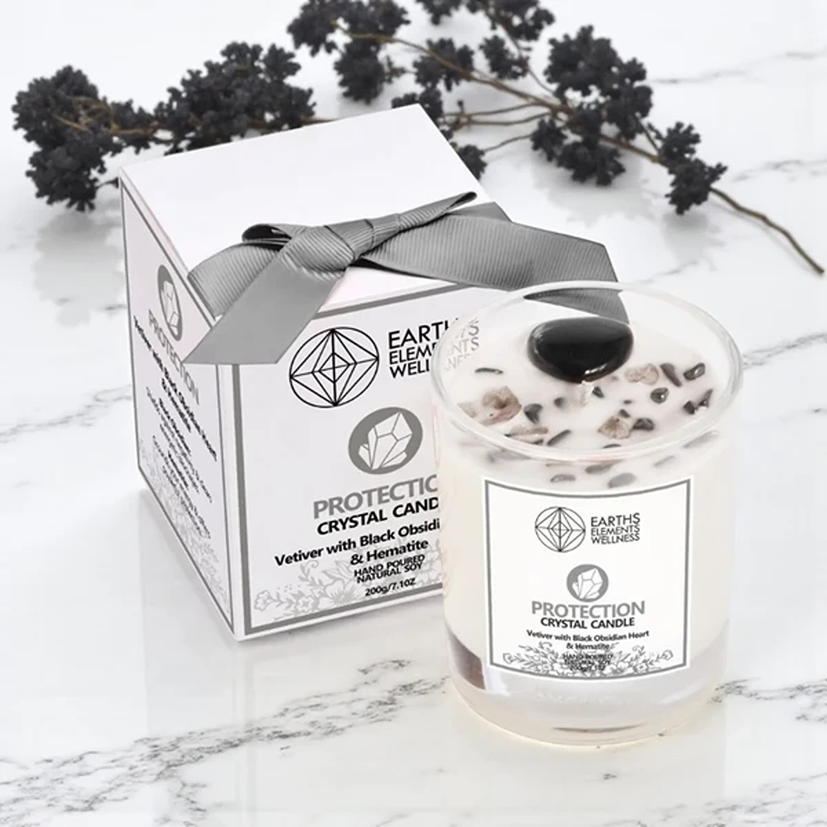 Earth's Elements Protection Crystal Candle with Vetiver scent, featuring a Black Obsidian heart and Hematite chips alongside its ribboned box.